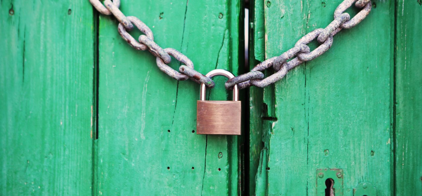 Bronze lock locking a chain across an old wooden door, painted green.