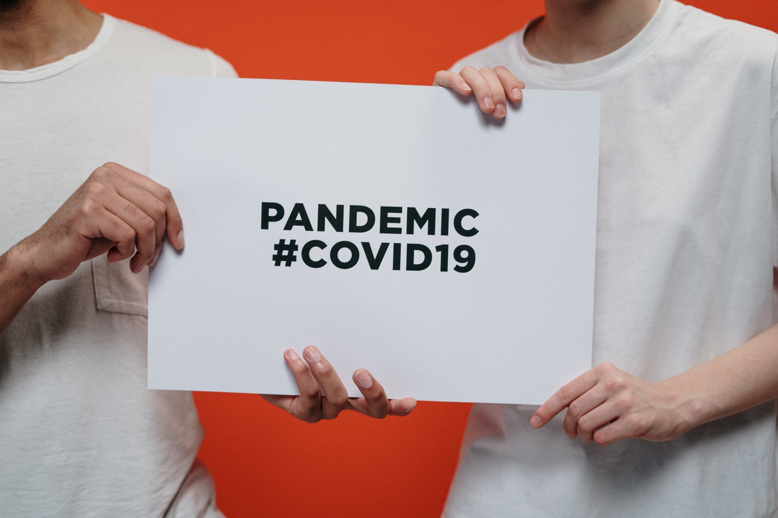 Two people in white T0shirts hold up a sign reading: "PANDEMIC #COVID19"